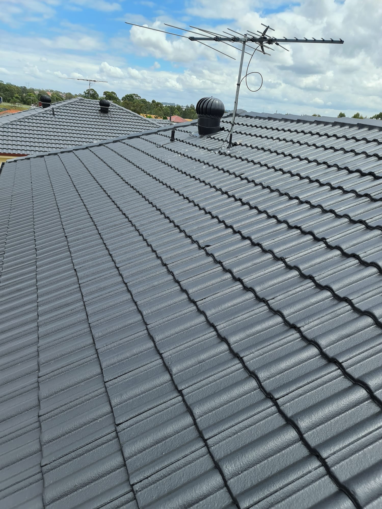 Newly coated charcoal tiled roof under a bright blue Sydney sky