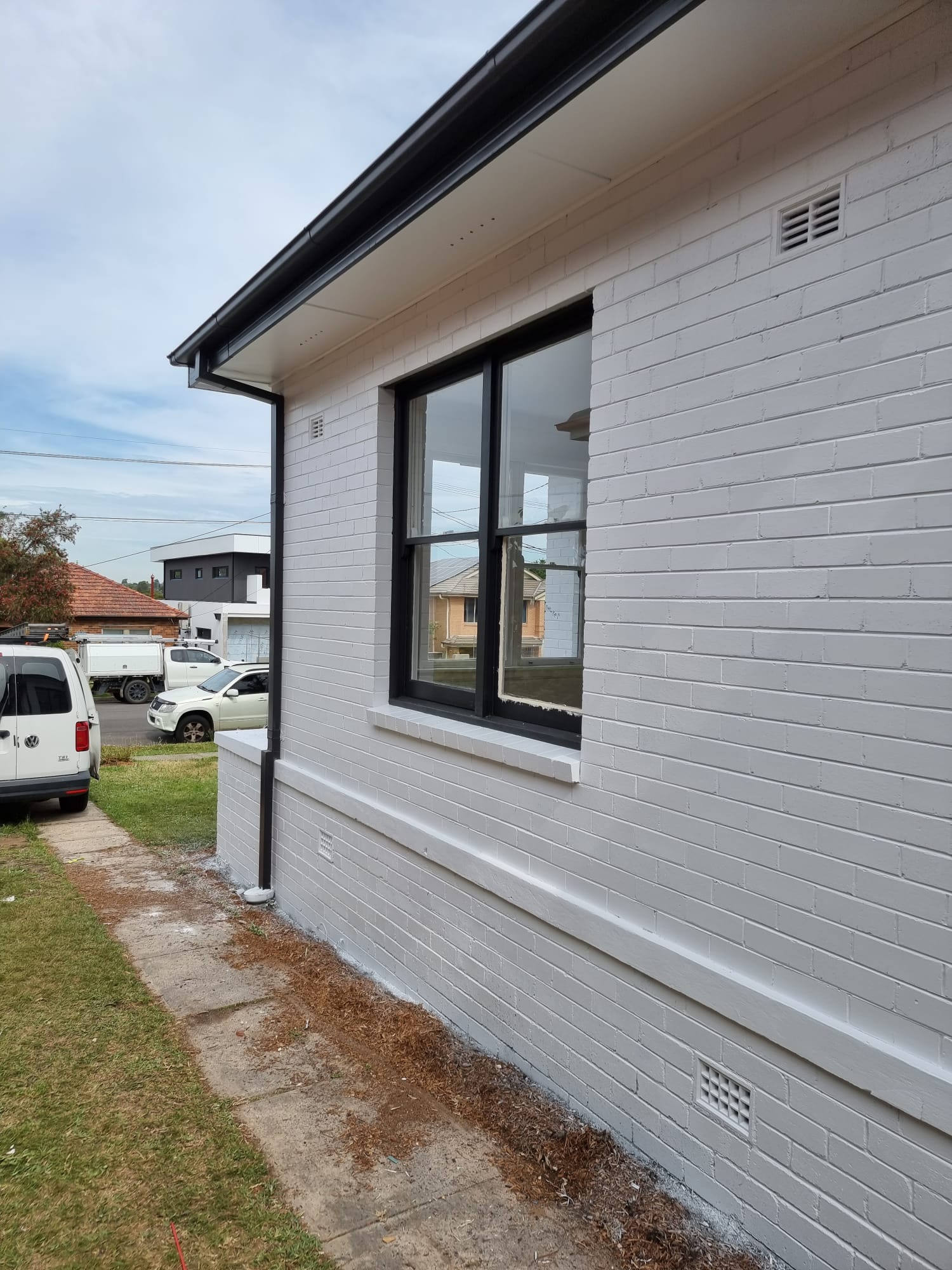 Rendered brick home repainted in soft grey with black trim under blue sky