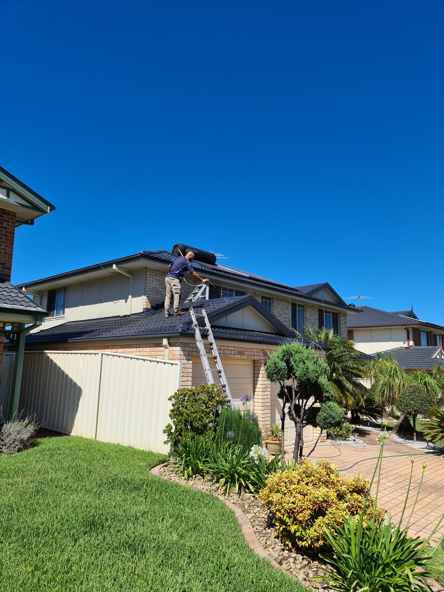 Maestro Painting tradesperson working on a roof under a clear blue Sydney sky